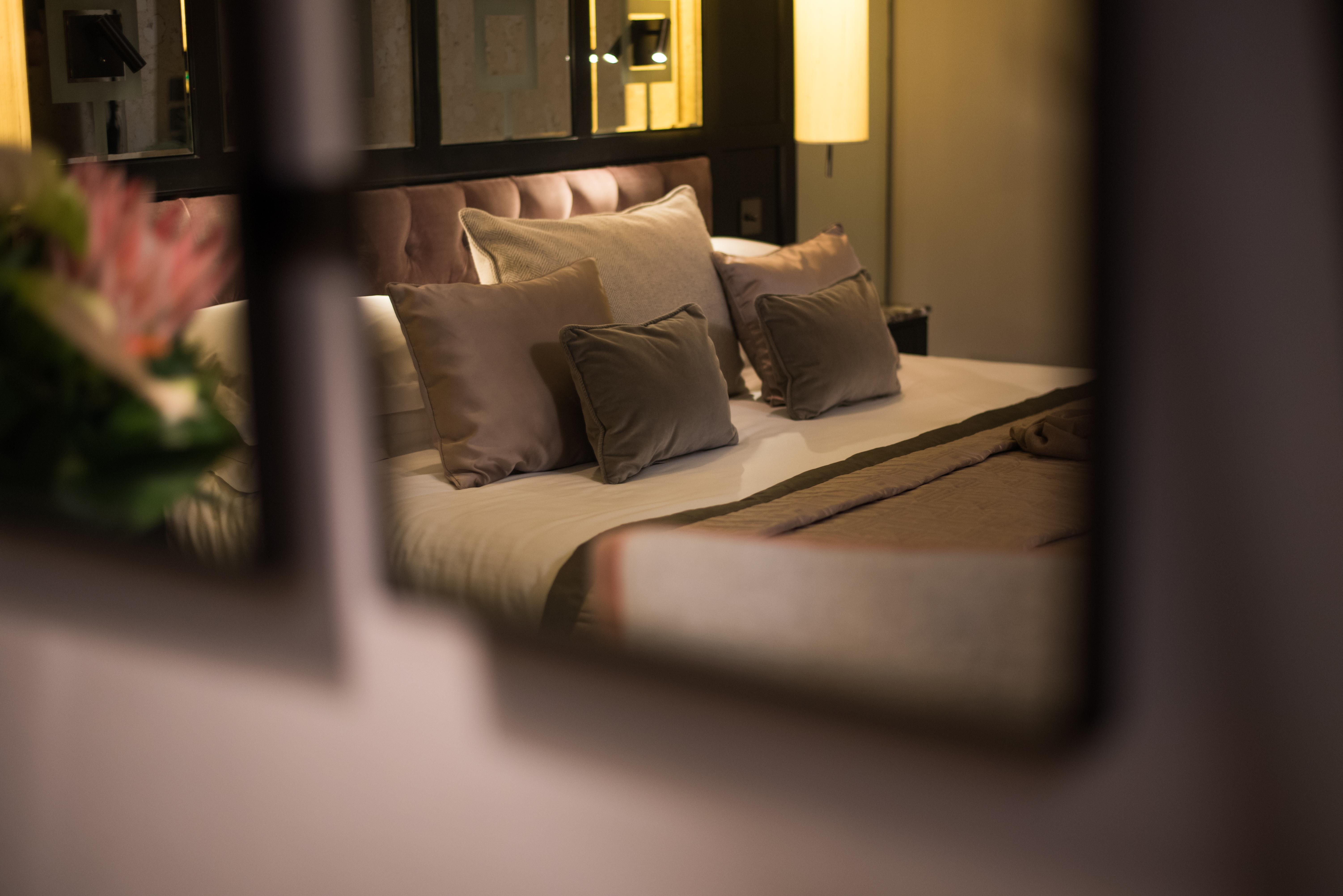 فندق ذا فيتزويليام بلفاست المظهر الخارجي الصورة The photo shows a cozy and elegantly decorated bedroom. The focal point is a plush bed with soft, neutral-colored bedding and several decorative pillows arranged neatly on it. The room has a warm ambiance, enhanced by a standing lamp that provides so