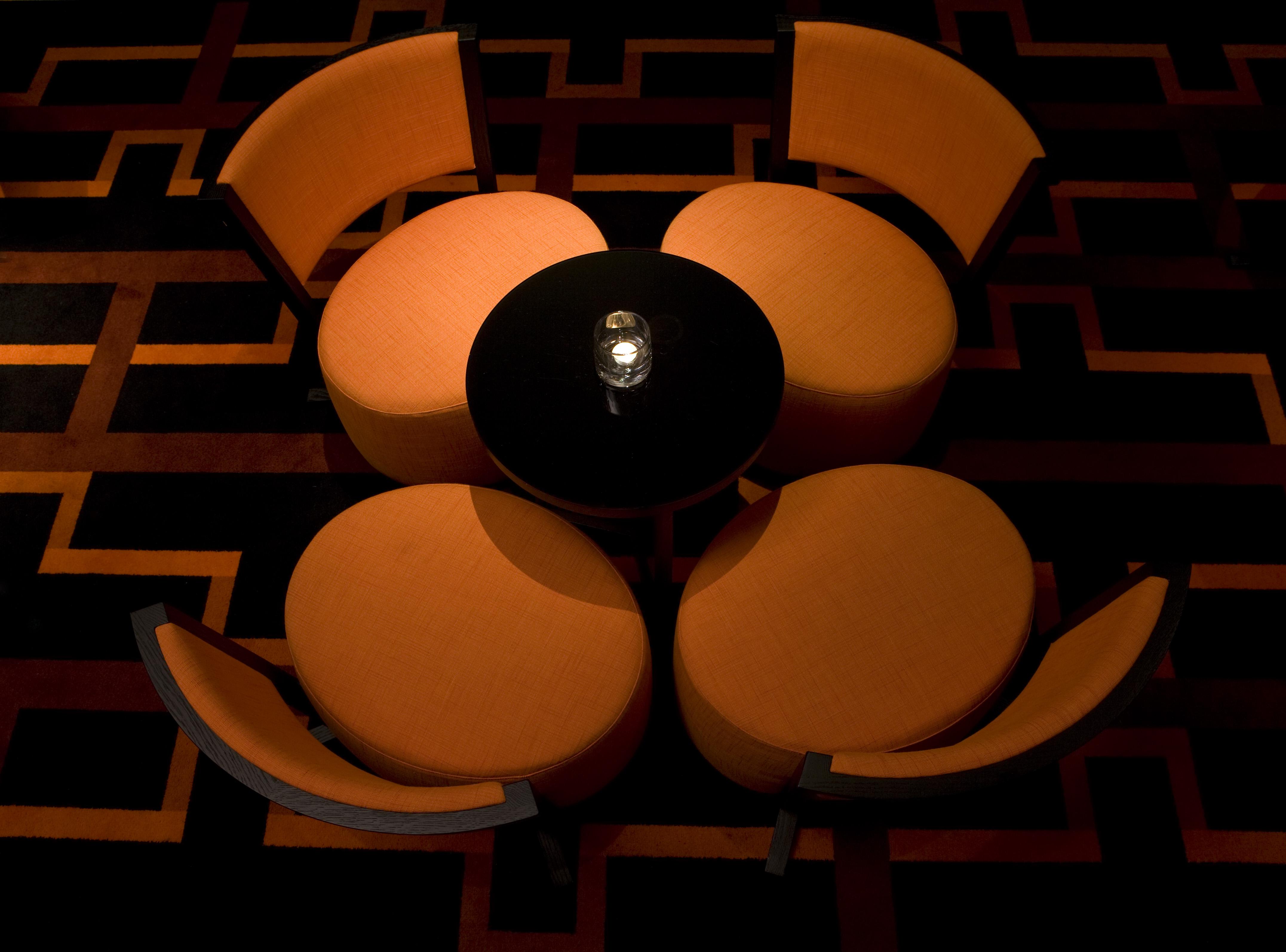 فندق ذا فيتزويليام بلفاست المظهر الخارجي الصورة The image shows a small seating arrangement consisting of four orange chairs arranged around a circular black table. The setting appears to be in a dimly lit area, emphasizing the warm tones of the chairs and the dark finish of the table. The floor d