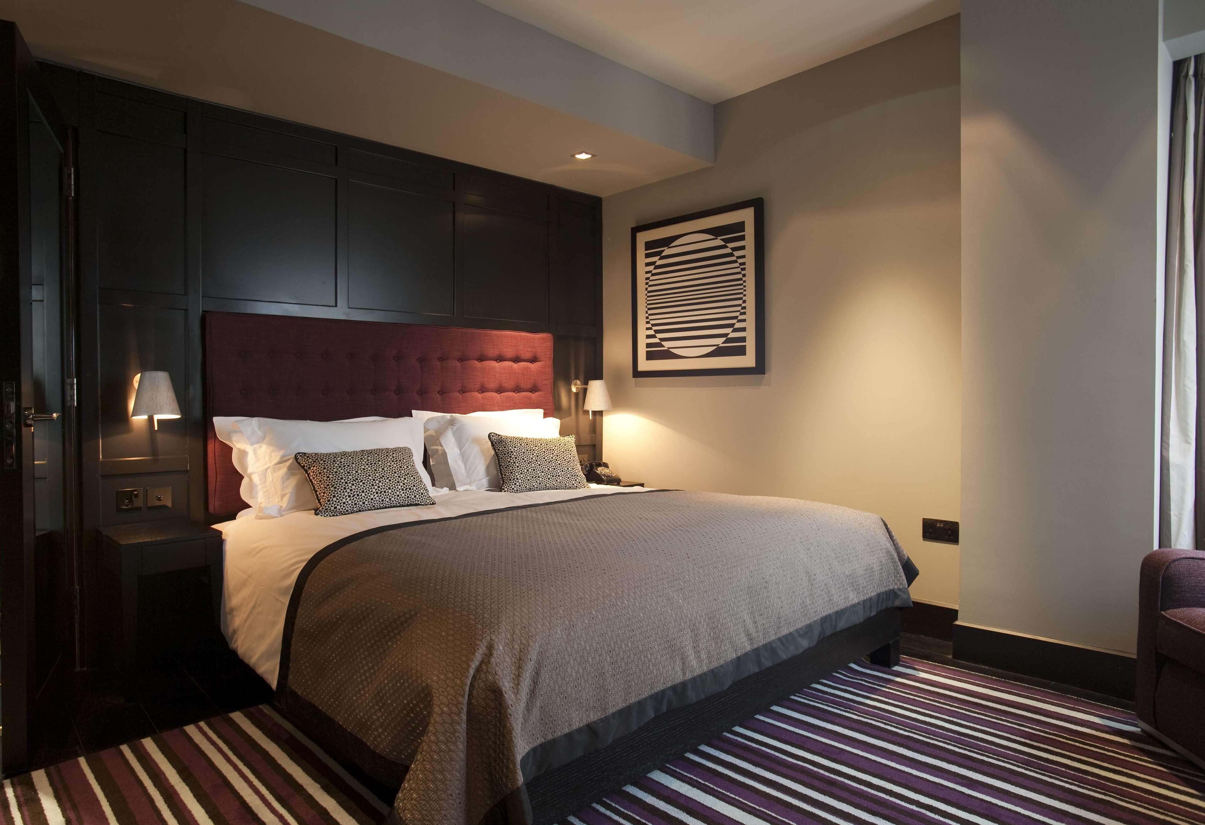 فندق ذا فيتزويليام بلفاست المظهر الخارجي الصورة The photo shows a stylish and modern hotel room. It features a large bed with a tufted headboard in a deep burgundy color. The bed is dressed with neutral-toned bedding and decorative pillows. On either side of the bed, there are small bedside lamps 